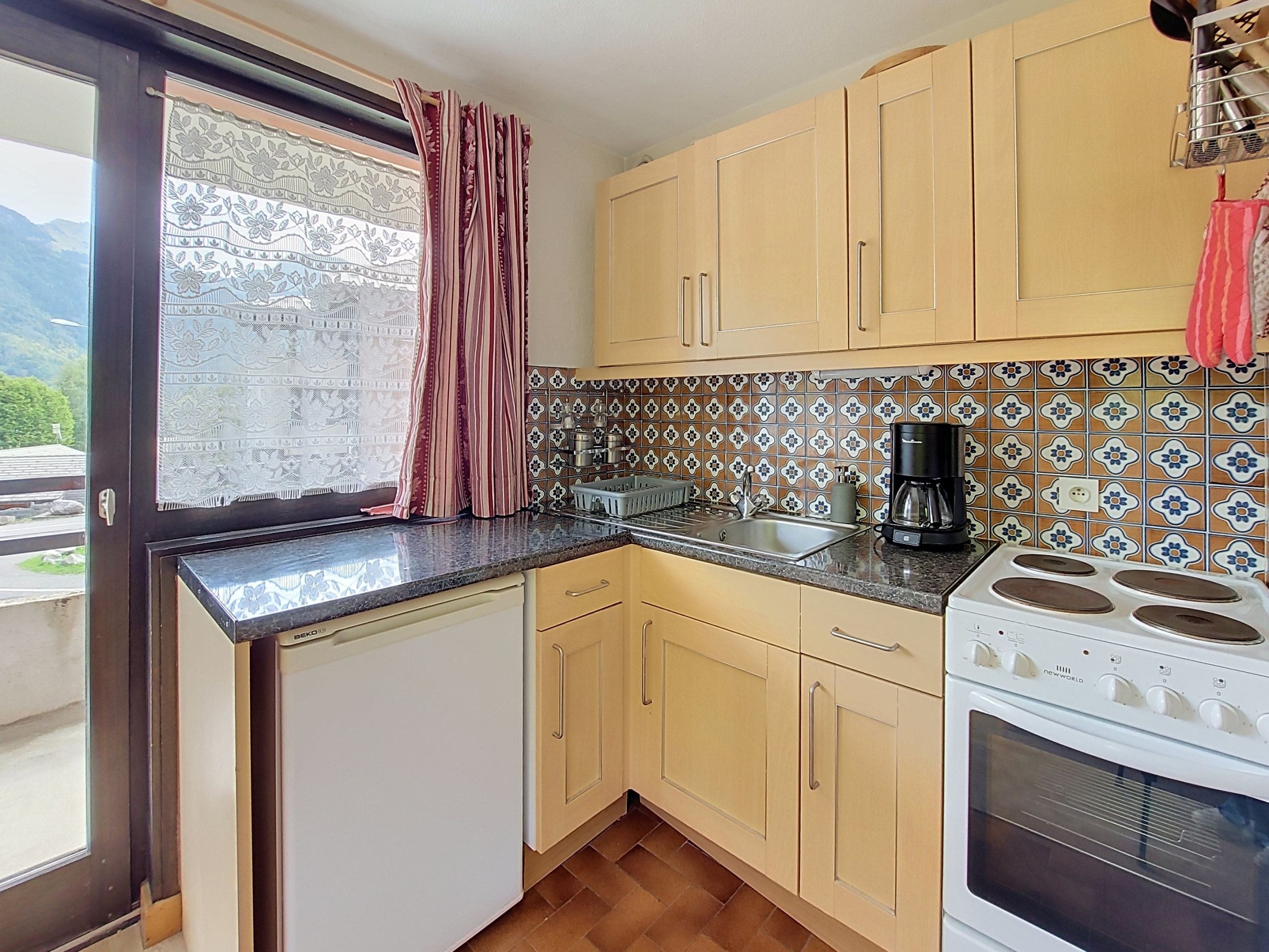A kitchen with a window, a sink, a stove, and a patterned backsplash.