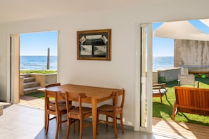 Una mesa y sillas de madera en una habitación con vista al mar a través de un puerta abierta.