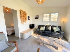Una sala moderna con un sofá, un televisor y una mesa de centro. Hay una cama en la habitación contigua y una ventana con vistas.