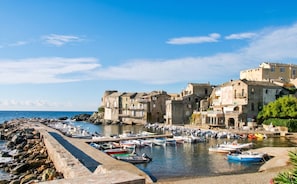 A coastal town with historic buildings, a rocky breakwater, and numerous boats docked at the harbor.