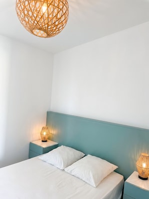 A bedroom with a bed, two bedside tables, and a hanging light fixture.