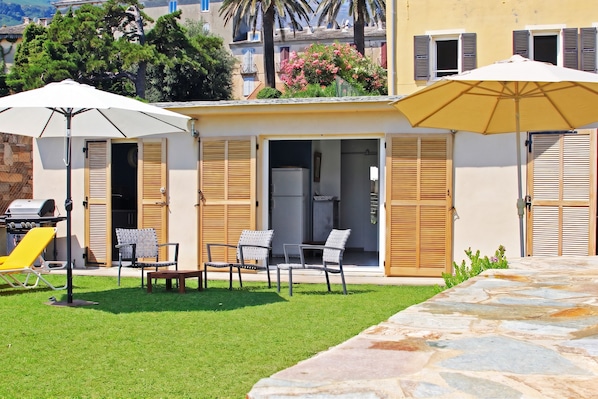 A villa with a patio area featuring outdoor furniture and umbrellas, a stone pathway, and a view of the surrounding landscape.