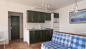A compact kitchen with dark cabinets, a white countertop, and a dining area with a checkered sofa. - One-Bedroom Apartment Sea View located 50m from the beach. (Rosas / Roses)