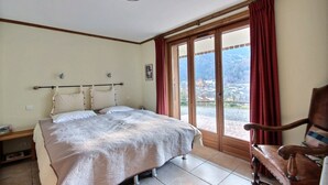 A bedroom with a bed, a chair, a window with curtains, and a view of a village. - CHALET WIFI - SAINT JEAN D'AULPS - 1 PEOPLE - TATOP (Saint-Jean-d´Aulps)