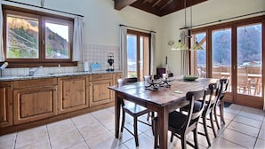 A kitchen with wooden cabinets, a large window, and a dining area with a table and chairs. - CHALET WIFI - SAINT JEAN D'AULPS - 1 PEOPLE - TATOP (Saint-Jean-d´Aulps)