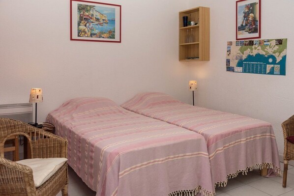 A room with two beds, wicker chairs, a shelf, and wall decorations including a map and framed pictures. - Le Lavandou, Charming cabin studio to rent for 4 people, sea view, steps from the beach (LE LAVANDOU)