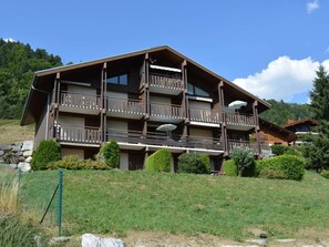 A multi-story building with balconies, surrounded by greenery and a clear sky.