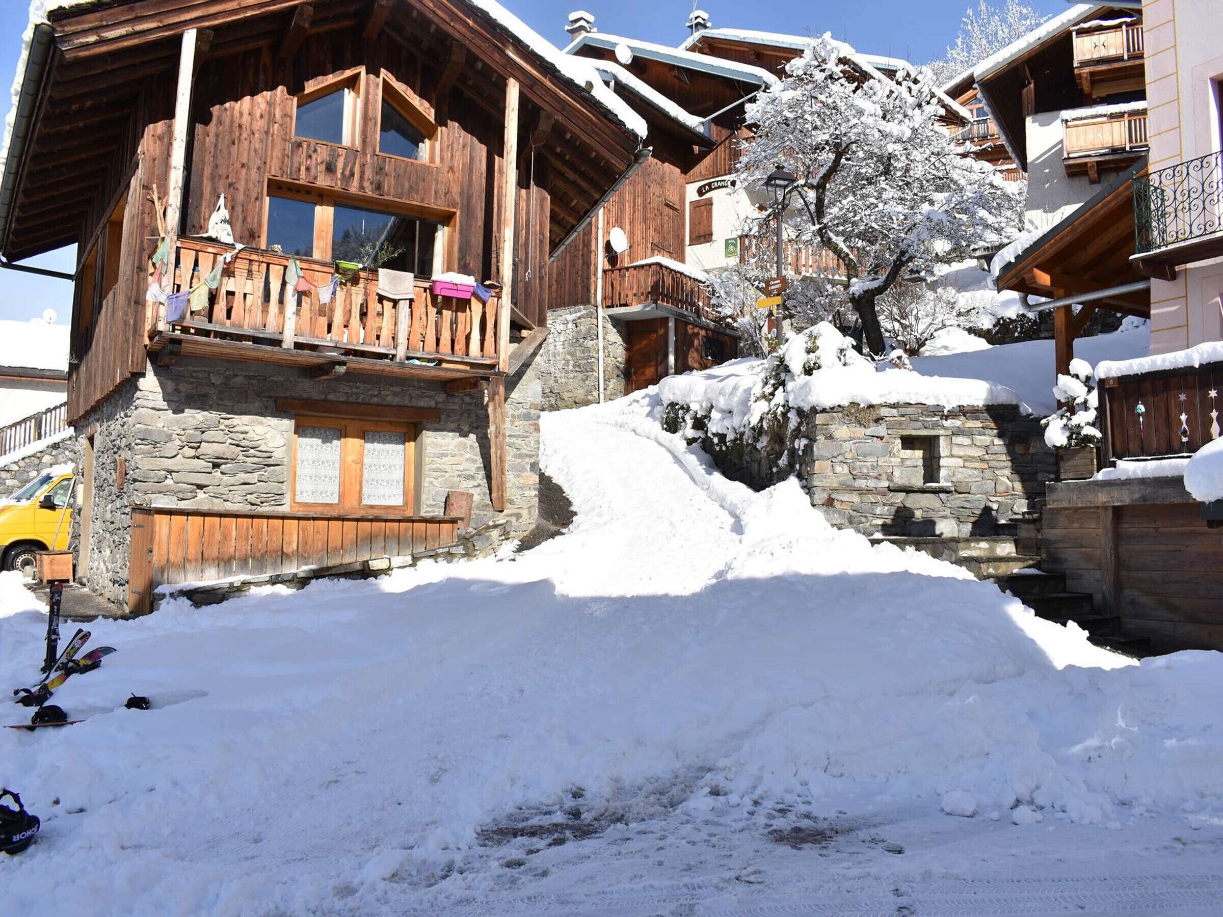 A wooden chalet with stone walls, a balcony with colorful items, and a snow-covered landscape.