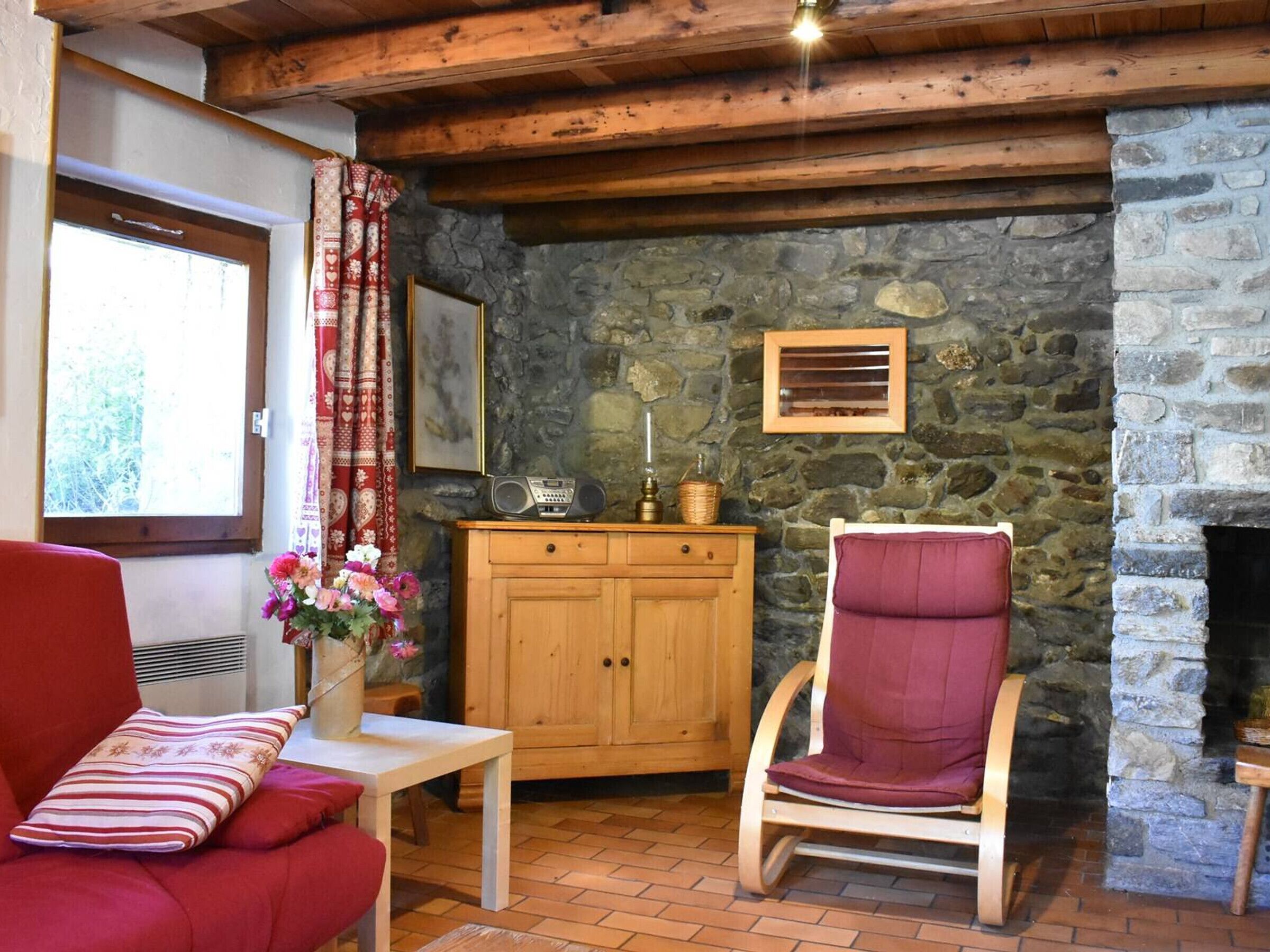 Una habitación acogedora con pared de piedra, muebles de madera, un sillón rojo, un armario de madera y una radio.