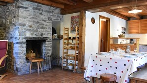 A rustic interior with a stone fireplace, wooden beams, a dining table set for four, and a kitchen area with wooden cabinets. - Traditional chalet for 8 in Méribel, calm and picturesque (Méribel)
