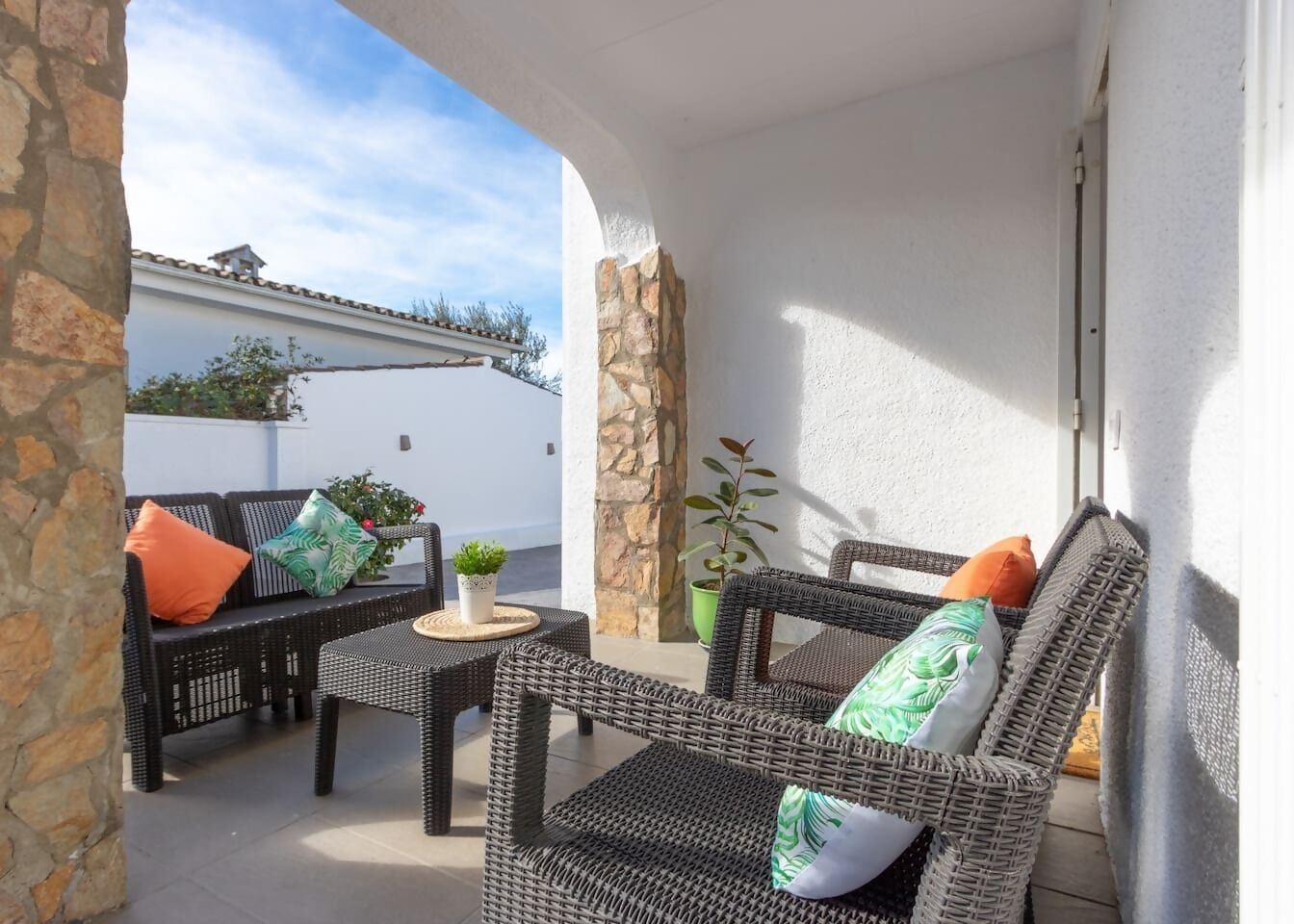 An outdoor patio with wicker furniture and potted plants.