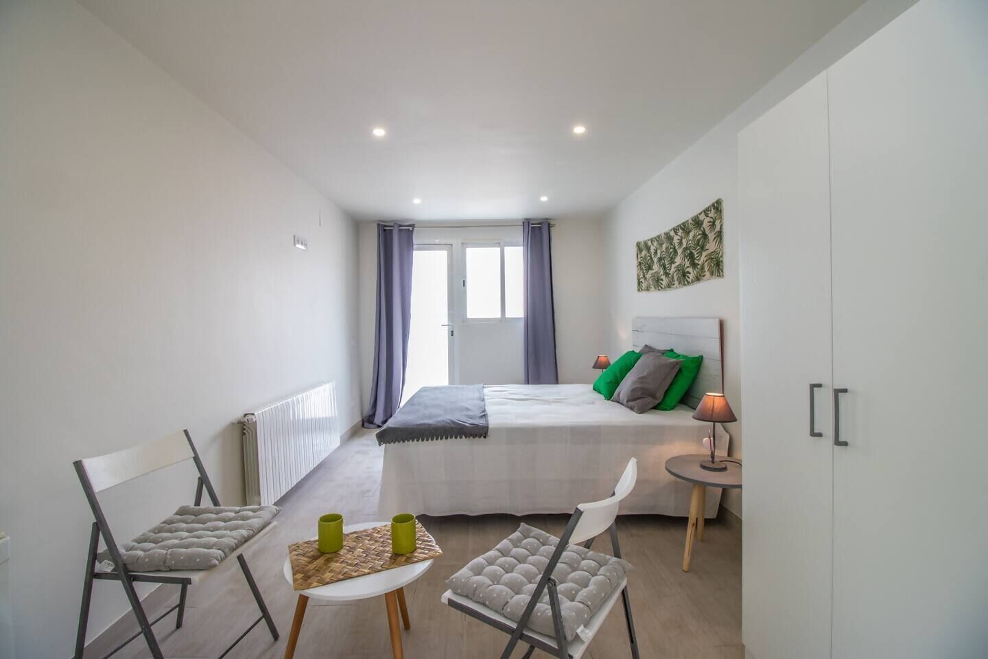 Une chambre à coucher de taille réduite, comprenant un lit, des lampes de chevet, une petite table et une chaise.
