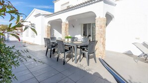 A patio with a table and chairs, a potted plant, and a stone pillar. - Piscina, mar y centro – Casa ideal para familias (Empuriabrava)