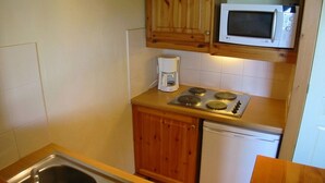 Une cuisine compacte dotée d’armoires en bois, d’un four à micro-ondes, d’une machine à café, d’une cuisinière et d’un lave-vaisselle.