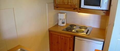 A compact kitchen with wooden cabinets, a microwave, a coffee maker, a stove, and a dishwasher.