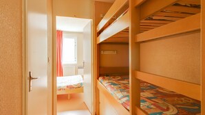 Un pasillo estrecho que lleva a una habitación con literas, una ventana con cortinas y un radiador.