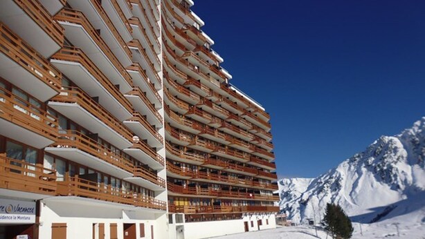Un hotel de varios pisos con balcones, una montaña nevada al fondo y un cielo despejado.