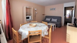 Un espacio habitable compacto con una mesa de comedor, sillas, sofá, kitchenette y un televisor pequeño.