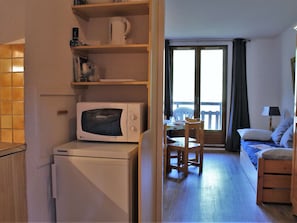 A compact room with a microwave, a small table with a chair, a bed, and a view through a window. - 3-room apartment in Risoul 1850 with balcony, pets allowed (Risoul)