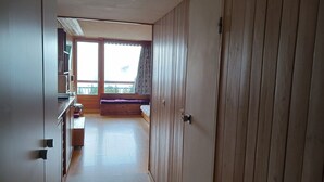 A room with a wooden door, a balcony with a view, and a kitchen area with cabinets and a countertop. - Studio 5 pers, ski-in/ski-out, near shops (Les Arcs 1800)