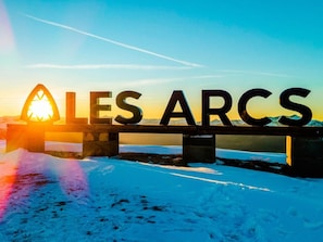 A bridge with the words "ALLES ARCS" in large letters, with a sun setting in the background.