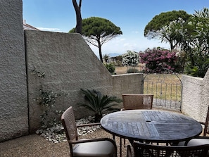 A patio with a round table and wicker chairs, surrounded by a stone wall and plants.