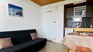 A compact living space with a black sofa, a small dining table with a patterned tablecloth, and a kitchenette with a microwave and coffee maker.