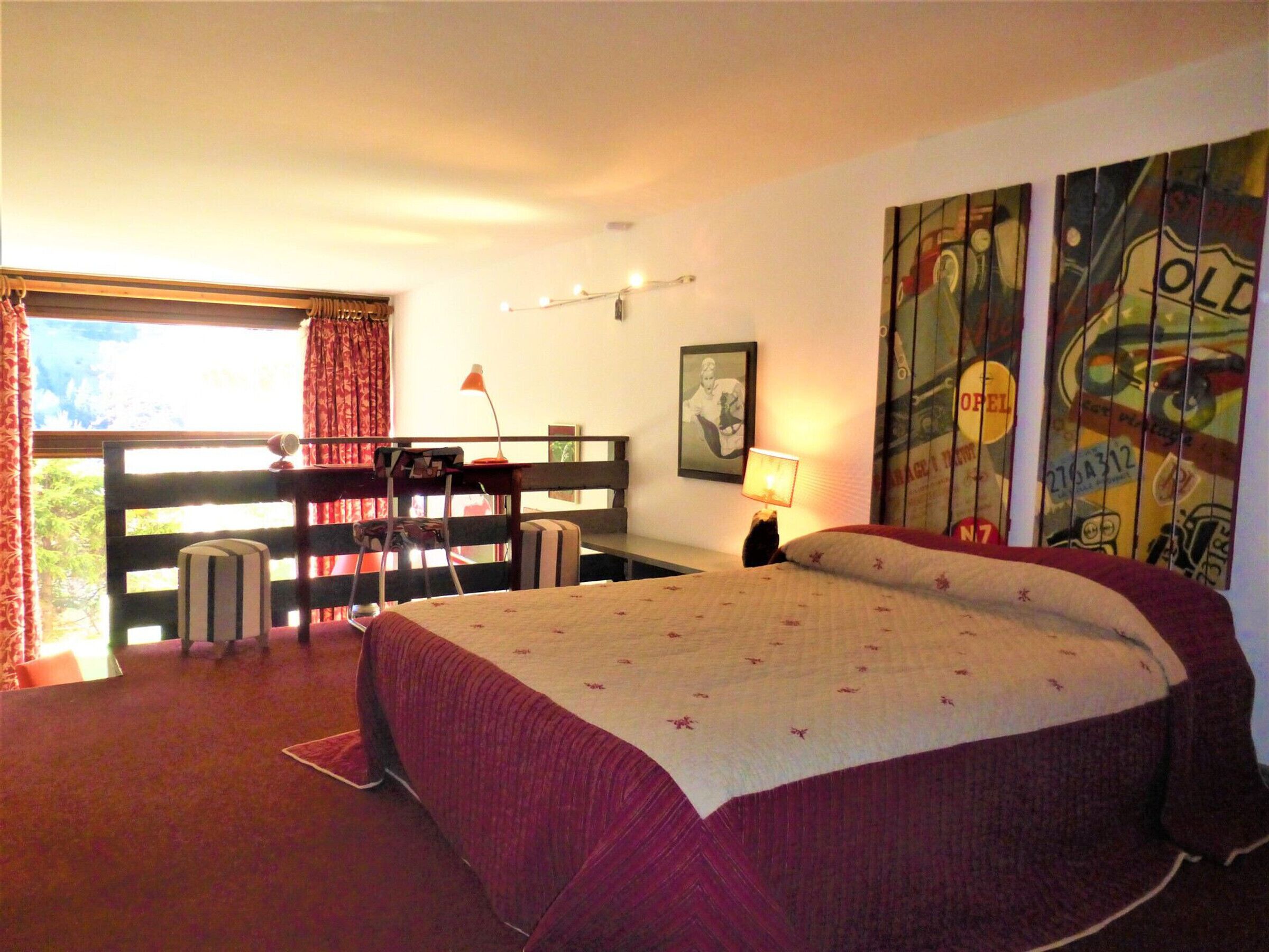 Une chambre à coucher avec un grand lit, un bureau, une chaise, une fenêtre avec des rideaux et un mur décoré de posters.
