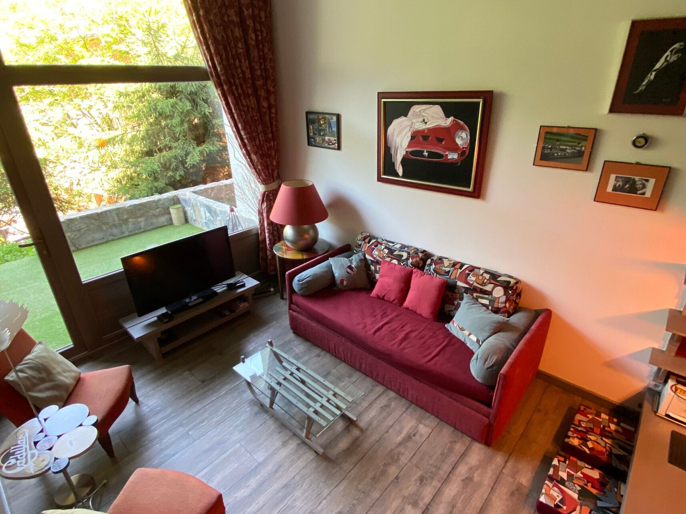 Un salon avec un canapé rouge, un téléviseur, une lampe et une fenêtre avec des rideaux.
