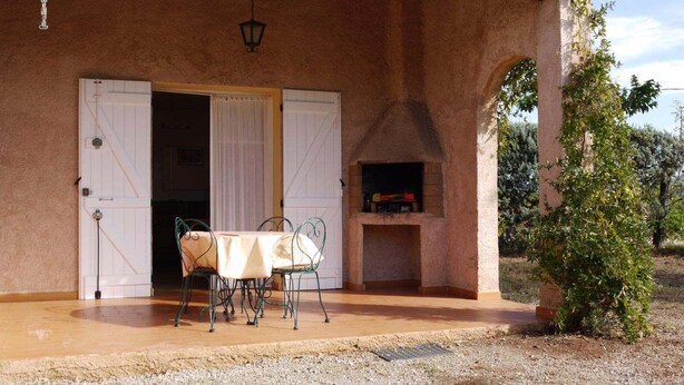 Un área de comedor al aire libre con mesa y sillas, una chimenea y un acceso cubierto.