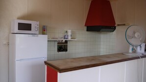 Una cocina con un refrigerador blanco, un microondas, una campana roja y un ventilador.