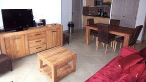 A living room with a TV, wooden furniture, a red sofa, and a kitchen in the background.