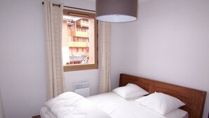A single bed with a wooden headboard, white bedding, and a window with curtains.