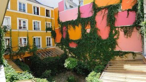 A courtyard with a wooden staircase, a small tree, and a building with yellow and pink walls partially covered in ivy. - C2D Green Valley (París)