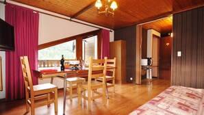 Una habitación con piso de madera, una cama con ropa de cama estampada, una mesa de comedor con sillas, una zona de cocina y un balcón con vistas.