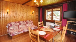 Un interior de madera con una mesa de comedor dispuesta para dos personas, un sofá y un televisor.