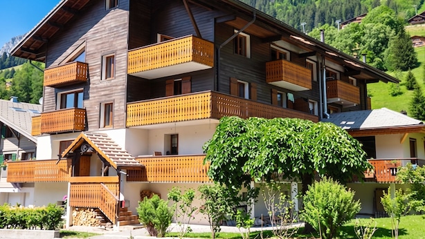Un edificio de madera de varios pisos con balcones, una escalera y un árbol en primer plano.