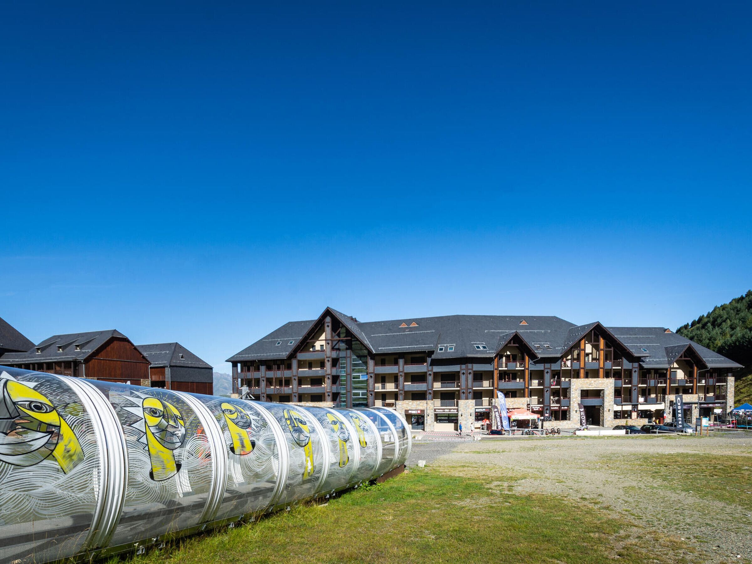 A hotel with multiple floors, balconies, and a large, cylindrical structure with artistic designs in the foreground.