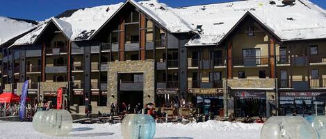 A multi-story hotel with a stone facade, balconies, and a ski slope in the background.