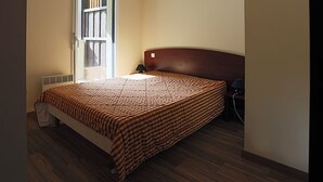Een slaapkamer met een bed, nachtkastje, lamp en een raam met jaloezieën.