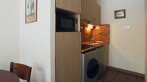 Een compacte keuken met houten kastjes, een magnetron, een spoelbak en een wasmachine.