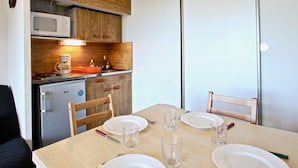 Una cocina compacta equipada con microondas, cafetera y un refrigerador pequeño. Hay una mesa de comedor con sillas y platos para dos personas.