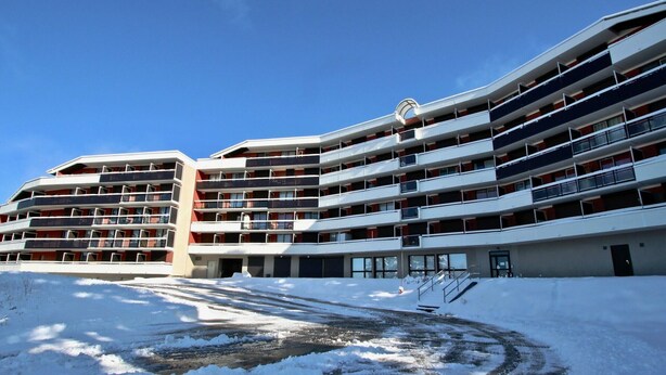 A multi-story hotel with a curved facade, balconies on each floor, and a snow-covered ground. - Functional studio for 4, pets allowed (Chamrousse)