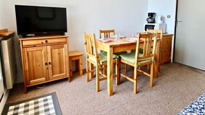 A dining area with a wooden table and chairs, a television on a wooden cabinet, and a coffee maker on the wall. - Functional studio for 4, pets allowed (Chamrousse)