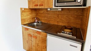 A compact kitchen with wooden cabinetry, a stainless steel sink, a microwave, and a small refrigerator. - Functional studio for 4, pets allowed (Chamrousse)