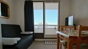 A compact room with a bed, a dining table with chairs, a television, and a sliding glass door leading to a balcony. - Functional studio for 4, pets allowed (Chamrousse)