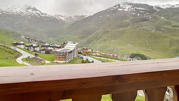 Paesaggio montuoso con un gruppo di edifici, probabilmente un albergo, circondato da dolci colline verdi e cime innevate.