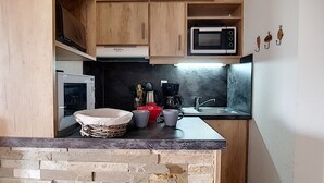 Una cucina compatta con mobili in legno, un forno a microonde, una macchina da caffè e una parete decorata con pietra.