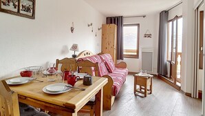 Una stanza accogliente con un tavolo da pranzo in legno apparecchiato per due persone, un letto con coperta a righe, una finestra con tende e un quadro appeso al muro.