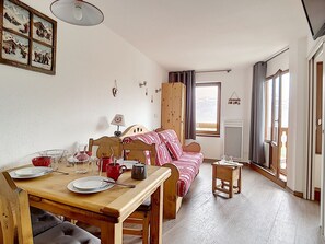 Una stanza accogliente con un tavolo da pranzo in legno apparecchiato per due persone, un letto con coperta a righe, una finestra con tende e un quadro appeso al muro.
